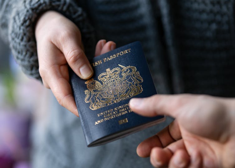 A hand giving a blue British passport to another hand